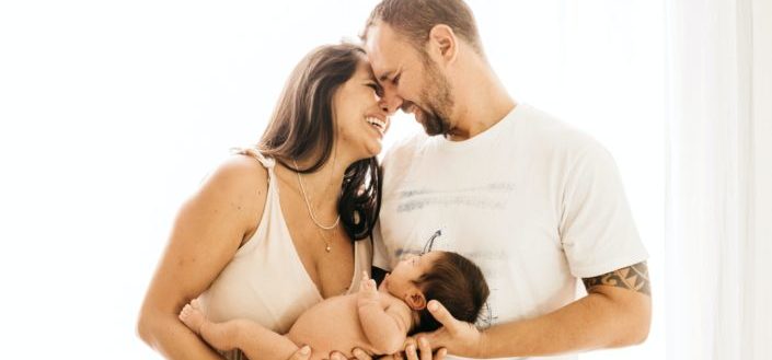 Una pareja sonriendo el uno al otro mientras sostiene a su bebé