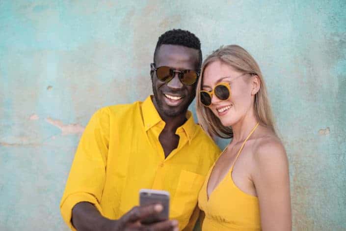 Piropos lindos y graciosos - Photo of smiling man in yellow shirt standing beside smiling woman in yellow spaghetti strap top looking at a phone