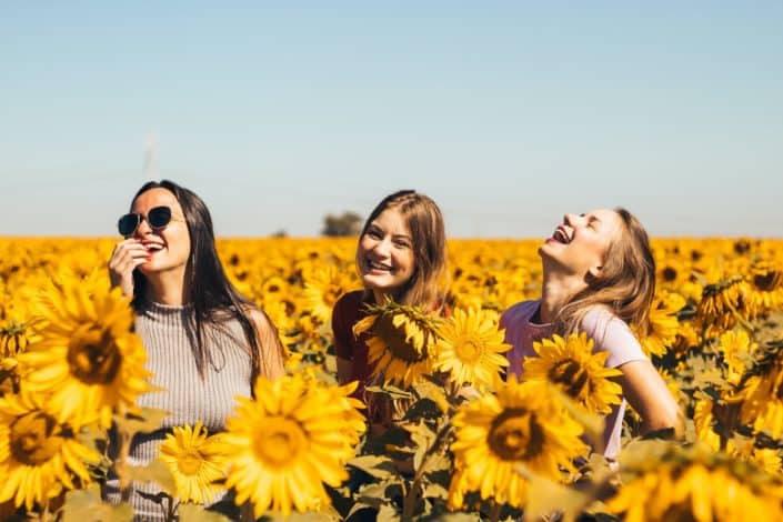 tres mujeres riendo en medio de un campo de girasoles