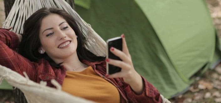 Chica sonriendo a su teléfono mientras está acostada en una hamaca