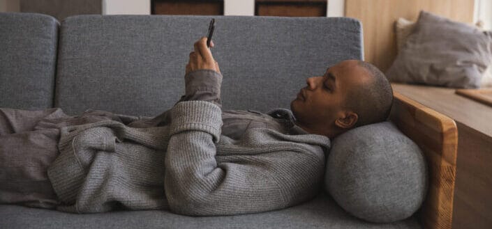 Hombre relajándose en su sofá mientras mira su teléfono