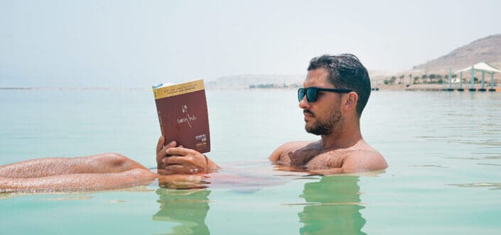 Hombre con gafas de sol leyendo un libro mientras está en el agua
