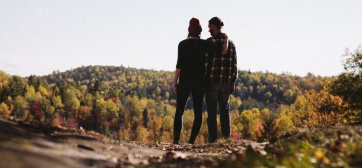 pareja de pie frente al campo de árboles verdes