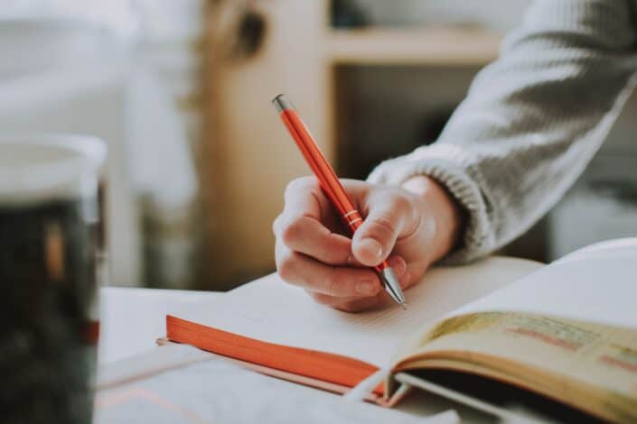  Hombre escribiendo en su cuaderno con un bolígrafo naranja