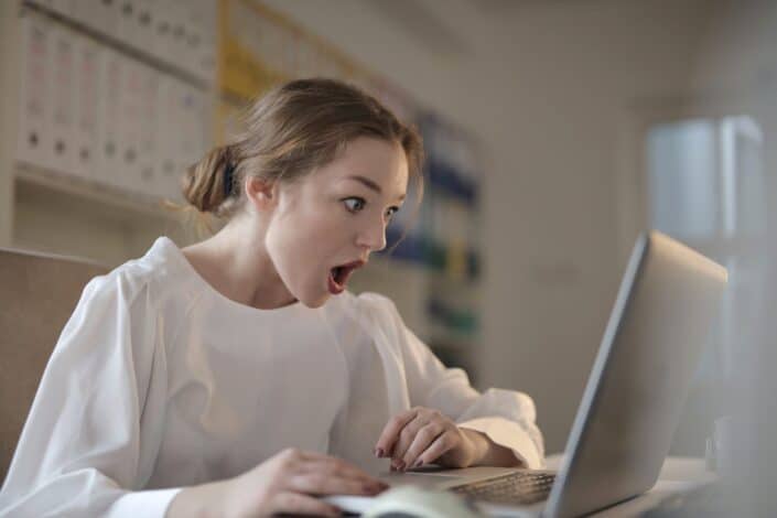 Mujer de blusa blanca usando una laptop plateada