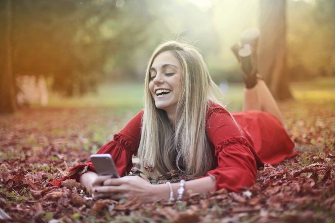 mensajes de amor para ella - Mujer tendida en el suelo llena de hojas secas mientras envia mensajes de texto