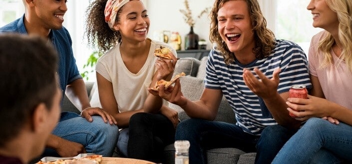Grupo de amigos multiétnicos comiendo pizza durante la fiesta en casa