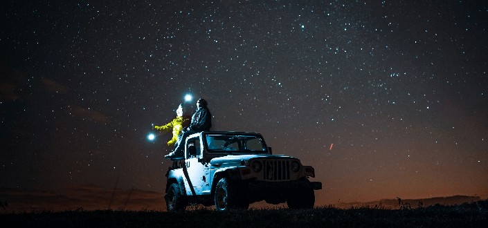 two people sitting on top of a cowboy looking at the sky at night