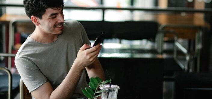smiling-young-man-browsing-smartphone-in-cafe-
