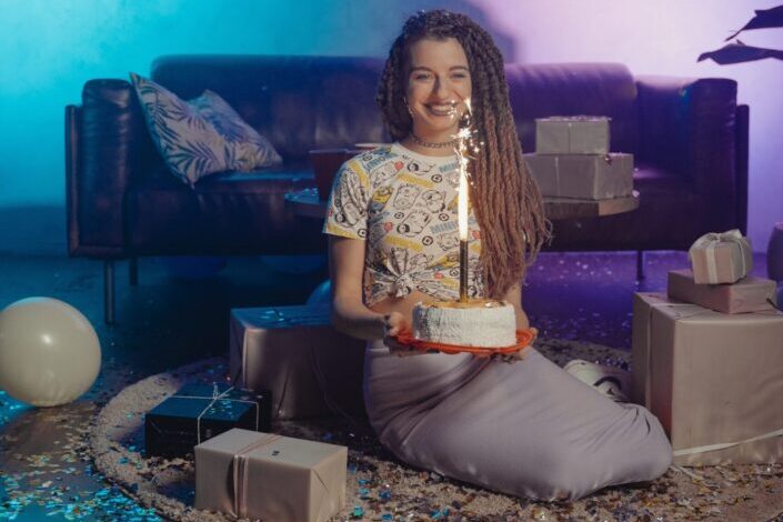 a-woman-sitting-on-a-carpet-with-confetti-and-gifts-while-holding-a-cake-